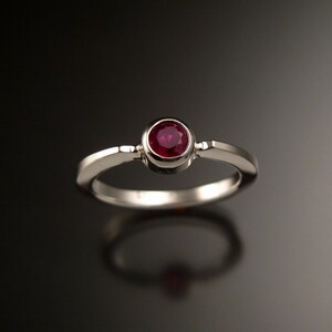 May include: A silver ring with a single round ruby gemstone set in a bezel setting.