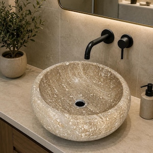 May include: A round, beige stone vessel sink with a textured, mottled surface and a central drain hole. The sink is mounted on a light-colored countertop and paired with a matte black wall-mounted faucet and a matching circular handle control.