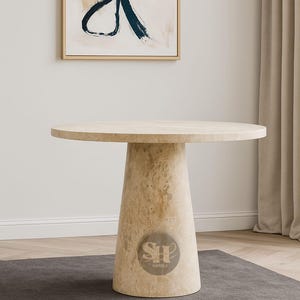 May include: A round, beige marble table with a conical base. The table has a smooth surface and a natural stone appearance. The base features a logo. An abstract painting hangs on the wall behind the table. The table is suitable for dining or display.