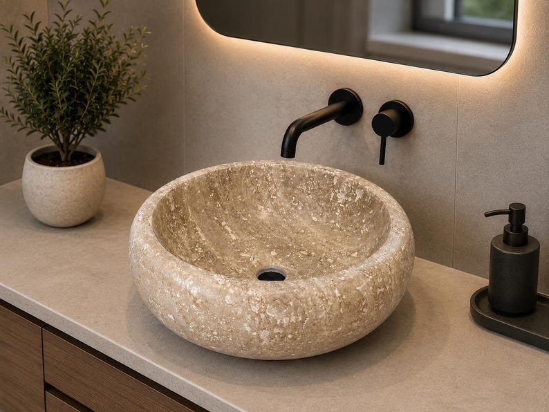 May include: A round vessel sink crafted from beige natural stone with a textured, mottled surface. The sink features a central drain hole and is paired with a matte black wall-mounted faucet and a matching black handle control fixture.
