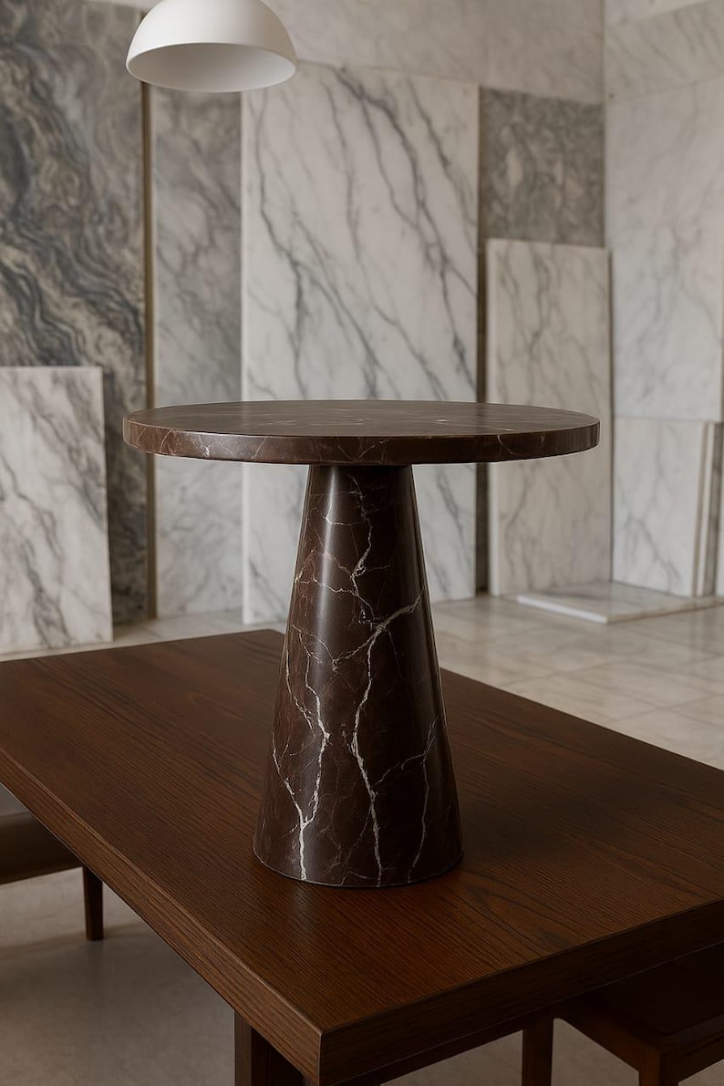 May include: A brown marble side table with a round top and a conical base. The table is set on a dark brown wooden surface. The marble has white veining. The table is approximately 20 inches in diameter and 24 inches tall.