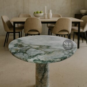 Puede incluir: Una mesa redonda de m&aacute;rmol con un patr&oacute;n veteado verde y blanco. La mesa tiene una base de pedestal cil&iacute;ndrica &uacute;nica. La mesa est&aacute; en un comedor con sillas y una mesa en el fondo.