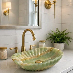 May include: A bathroom sink with a green and gold onyx basin. The sink has a gold faucet and fixtures. Two wall sconces with white shades flank a mirror. A small fern in a white pot sits on the counter.