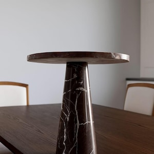 May include: A brown marble side table with a round top and a conical base. The table has white veining throughout the dark brown marble. The table is approximately 20 inches in diameter and 24 inches tall.