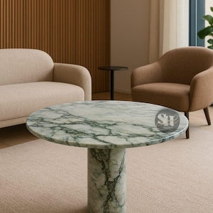 May include: A circular coffee table with a marble top, displaying green veining. The table has a cylindrical base and is placed on a neutral-toned rug. The room also features a beige sofa and armchair.