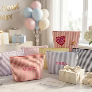 Peut inclure: Une collection de pochettes zippées en tissu seersucker à rayures verticales de différentes couleurs, dont rouge, bleu, jaune et violet. Deux pochettes portent des noms brodés, Olga et Thea, et une autre présente un écusson en forme de cœur.