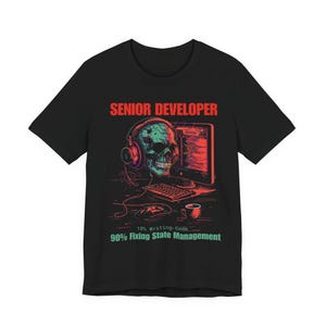 Puede incluir: Camiseta negra con un gráfico de una calavera con auriculares, junto con un monitor de ordenador, teclado y ratón. El texto "SENIOR DEVELOPER" está encima del gráfico, y "10% writing-code, 90% Fixing State Management" está debajo.