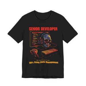 Puede incluir: Camiseta negra con un gráfico de una calavera con auriculares, un monitor de ordenador, un teclado y una taza de café. El texto "SENIOR DEVELOPER" está encima del gráfico, y "10% Writing Code, 90% Fixing State Management" está debajo.