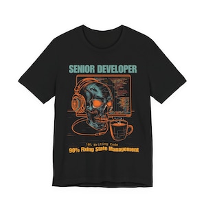 May include: Black t-shirt featuring a skull wearing headphones, with a computer screen displaying code. The text "SENIOR DEVELOPER" is above the skull, and "10% Writing Code, 90% Fixing State Management" is below.