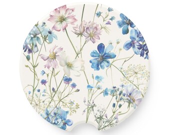Könnte beinhalten: Ein weißer Keramik-Untersetzer mit einem Blumendesign mit blauen, rosa und weißen Blumen. Der Untersetzer hat einen Ausschnitt in Form eines Getränkehalters für das Auto.