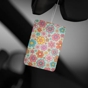 Könnte beinhalten: Ein Auto-Lufterfrischer mit einem Blumenmuster. Das Design zeigt eine Vielzahl von bunten Blumen auf hellblauem Hintergrund.