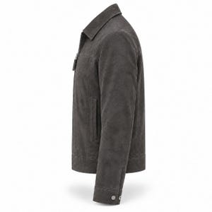K&ouml;nnte beinhalten: Eine anthrazitfarbene Wildlederjacke mit klassischem Kragen, durchgehendem Frontrei&szlig;verschluss mit rechteckigem Zipper, langen &Auml;rmeln mit gekn&ouml;pften Manschetten und einem geraden Saum. Die Jacke hat eine glatte, matte Textur und eine klare Passform.