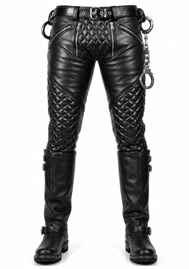 May include: Black leather trousers featuring quilted panels on the thighs and crotch, silver-tone zippered pockets, a belt with a metal buckle, and a silver-tone metal chain with attached handcuffs hanging from the side of the waistband.
