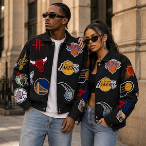 May include: Two black denim jackets featuring various embroidered NBA team logos and basketball graphics. The jackets have a collared neckline, metal button closures, and long sleeves. Each jacket is adorned with multiple colorful patches representing professional basketball teams, including the Lakers, Knicks, and Bulls, arranged across the front and sleeves.