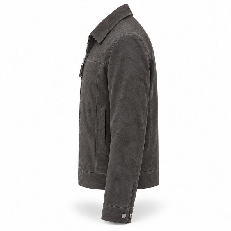 K&ouml;nnte beinhalten: Eine anthrazitfarbene Wildlederjacke mit klassischem Kragen, durchgehendem Frontrei&szlig;verschluss mit rechteckigem Zipper, langen &Auml;rmeln mit gekn&ouml;pften Manschetten und einem geraden Saum. Die Jacke hat eine glatte, matte Textur und eine klare Passform.