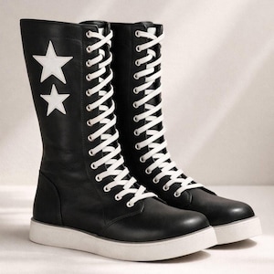 Peut inclure: Bottes en cuir noir avec des étoiles blanches et des lacets blancs. Les bottes ont une semelle blanche et une hauteur mi-mollet. Chaussures élégantes et audacieuses.