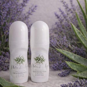 Könnte beinhalten: Zwei weiße Roll-on-Deo-Flaschen mit floralem Design und Text. Der Hintergrund besteht aus Lavendelblüten und Aloe-Vera-Blättern, was eine natürliche und frische Ästhetik erzeugt.