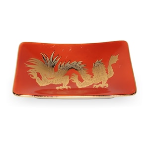 Puede incluir: Un plato rectangular de cerámica roja con un diseño de dragón dorado. El dragón está centrado en el plato y tiene detalles intrincados. El plato tiene un borde dorado. El diseño es ornamentado y elegante.
