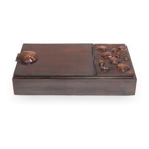 Peut inclure: Une boîte rectangulaire en bois brun foncé avec un couvercle à charnière. La boîte a une poignée en forme de coquillage. Le couvercle est orné d'un relief en forme de coquillages. La boîte est probablement destinée au rangement ou à l'exposition.