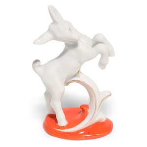 May include: A white ceramic deer figurine in a leaping pose, accented with gold trim. The deer is mounted on a vibrant orange base with a decorative swirl. A charming decorative piece.