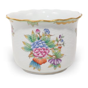 Könnte beinhalten: Weißer Keramik-Blumentopf mit gewelltem Rand und goldenem Zierrat. Der Topf hat ein farbenfrohes Blumendesign mit blauen, rosa, orangefarbenen und lila Blumen und grünen Blättern. Ein dekoratives Stück für Zimmerpflanzen.