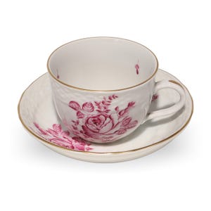 May include: A white teacup and saucer set with a floral rose design in shades of pink. The cup and saucer have gold trim. The cup has a textured surface. The set is designed for tea or coffee.