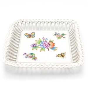 May include: A white, square woven basket with a matching square ceramic insert. The insert features a floral and butterfly design in shades of pink, blue, orange, and yellow. The basket has a decorative, open weave.