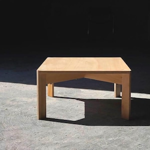 Könnte beinhalten: Ein helles, quadratisches Couchtisch aus Holz mit vier stabilen Beinen. Der Tisch ist aus hellfarbenem Holz gefertigt und vor einem dunklen Hintergrund platziert. Der Tisch ist ca. 76 cm lang und breit sowie 46 cm hoch.