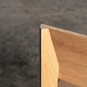 May include: Close-up of the corner of a wooden chair with a light brown finish. The chair has a simple, modern design.
