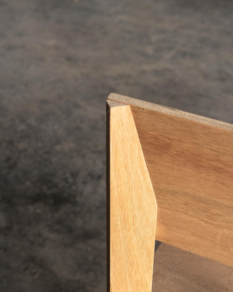May include: Close-up of the corner of a wooden chair with a light brown finish. The chair has a simple, modern design.