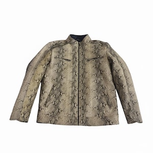 Może przedstawiać: Kurtka ze wzorem skóry węża z czarnym kołnierzem i zamkiem błyskawicznym. Kurtka posiada dwie kieszenie na piersi zapinane na zamek oraz zapięcie na zamek błyskawiczny na całej długości. Neutralne odcienie wzoru skóry węża tworzą wszechstronną odzież wierzchnią.