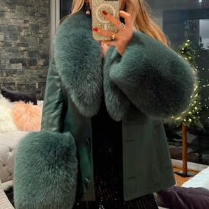 May include: A dark green leather coat with a matching fur collar and cuffs. The coat has a button-down front and is worn with black pants. The fur appears soft and luxurious, creating a stylish and elegant look.