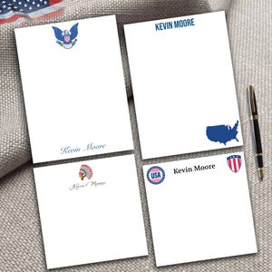 May include: Four white notepads with patriotic designs and the name "Kevin Moore" printed on them. One notepad features a blue eagle, another a map of the USA, a third an American Indian headdress, and the last a USA emblem.