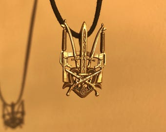 May include: A gold-colored pendant necklace featuring a stylized trident with crossed rifles and a sword. The pendant is on a black cord.