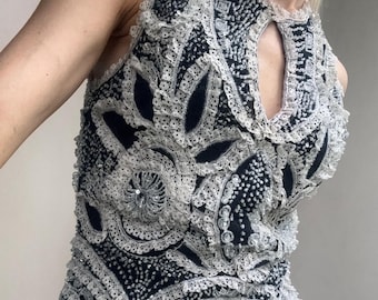 Può includere: Top nero senza maniche con intricati ricami di pizzo bianco e paillettes. Il top presenta uno scollo a goccia e una gonna color crema. Il design include motivi floreali e geometrici, creando un'estetica vintage o retrò.