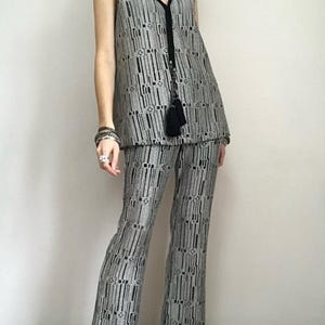May include: A two-piece outfit comprising a sleeveless vest and flared trousers. The outfit is patterned with vertical black and silver stripes and geometric shapes. The vest has a V-neck with black trim and a tassel. The trousers are high-waisted.