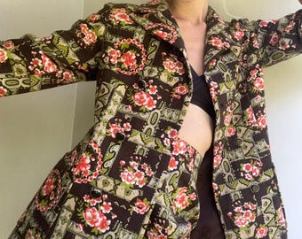 May include: A vintage two-piece outfit with a brown floral print. The jacket is double-breasted with black buttons. The skirt matches the print. The floral pattern includes red and pink flowers with green accents.