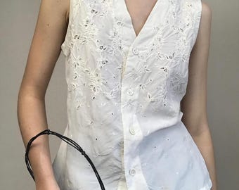 Può includere: Gilet bianco senza maniche con ricami floreali e chiusura con bottoni. Il gilet ha uno scollo a V ed è realizzato in tessuto leggero. Capo d'abbigliamento vintage.