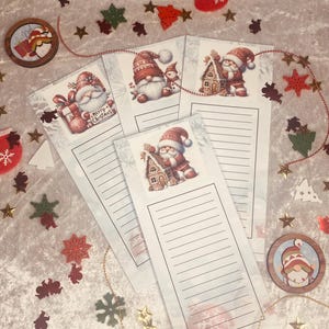 May include: A collection of Christmas-themed stationery, including lined notepads with Santa Claus and gnome illustrations. Decorative elements like stars, snowflakes, and a red stocking are scattered around the notepads. Two wooden coasters with gnome designs are also visible.