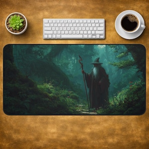 May include: A rectangular desk mat featuring a printed illustration of a wizard with a long white beard, a pointed hat, and a wooden staff standing on a path within a dense, dark green forest with lush foliage and tall, shadowed trees.