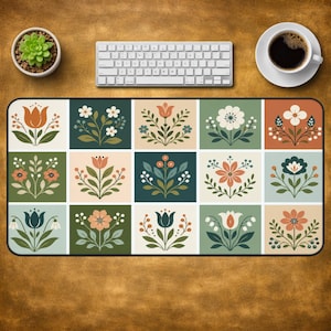 Può includere: Un tappetino da scrivania rettangolare con una griglia di quindici pannelli quadrati, ognuno dei quali mostra un'illustrazione botanica unica di fiori, foglie e bacche in una tavolozza di verde, arancione, crema e verde acqua scuro con bordo nero.