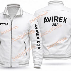 Puede incluir: Chaqueta de cuero blanca con la marca "AVIREX" impresa en negro en la parte delantera y trasera. La chaqueta tiene cierre de cremallera, dos bolsillos delanteros y "AVIREX USA" impreso en las mangas.