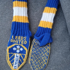 Może przedstawiać: Para dzianinowych skarpet w kolorze niebieskim, żółtym i białym. Skarpety mają napis "LEEDS UNITED" i herb drużyny. Podeszwy mają żółto-niebieski wzór w romby.