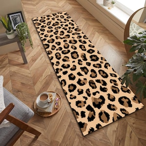 May include: A rectangular beige rug with a leopard print pattern in black and brown. The rug is placed on a wooden floor. The rug is a decorative item for a home.