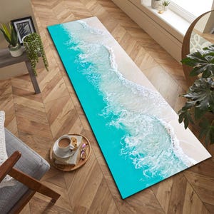 Könnte beinhalten: Ein rechteckiger Teppich mit einer Strandszene. Er zeigt türkisfarbenes Ozeanwasser, das auf einen sandigen Strand trifft, mit weißen, schäumenden Wellen. Der Teppich liegt auf einem Holzboden und schafft ein Küstenmotiv.