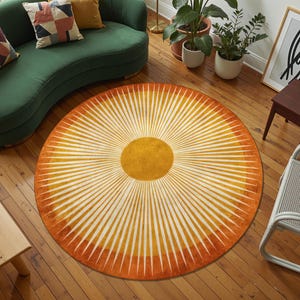 May include: A round rug with a sunburst design. The rug features a central yellow circle with radiating white and orange stripes. The rug is placed on a wooden floor, and the room includes a green sofa and plants.