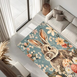 May include: A blue and white floral rug with a brown rabbit and colorful Easter eggs. The rabbit is looking at the viewer with its ears perked up.