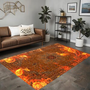 May include: A large, rectangular area rug with an intricate, ornate design in shades of orange, yellow, and brown. The rug features a central medallion with a swirling pattern and a border of smaller motifs. The rug is laid out on a hardwood floor in a living room setting.