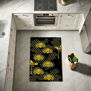 May include: Black and gold kitchen rug with a honeycomb pattern and bees. The bees are outlined in gold and have a dripping honey effect.