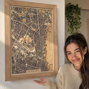 Könnte beinhalten: Eine rechteckige Wandkarte aus Holz von Bogota mit komplizierten lasergeschnittenen Straßenmustern und topografischen Details. Die Karte ist in einen hellen Holzrahmen gefasst und zeigt den Stadtnamen Bogota unten in der Mitte.